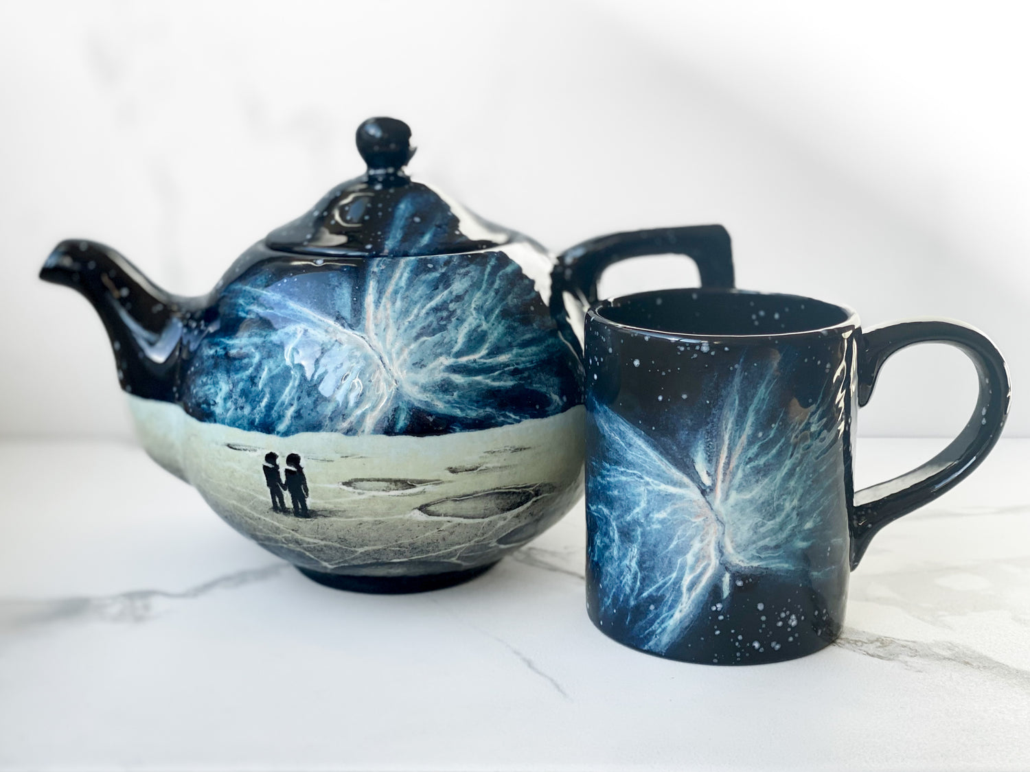 Teapot and Mug featuring the Butterfly Nebula. Teapot features cratered landscape below nebula with two astronauts holding hands.
